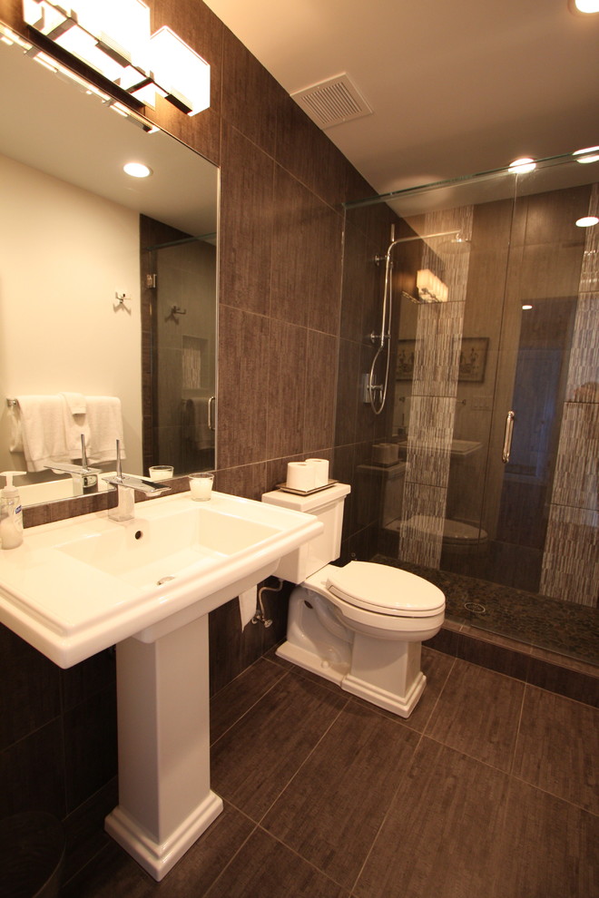 Bild på ett mellanstort orientaliskt badrum med dusch, med en dubbeldusch, en toalettstol med separat cisternkåpa, brun kakel, porslinskakel, bruna väggar, klinkergolv i porslin, ett piedestal handfat, brunt golv och dusch med gångjärnsdörr
