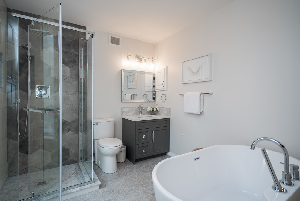 This is an example of a medium sized contemporary ensuite bathroom in Other with shaker cabinets, grey cabinets, a freestanding bath, a corner shower, a two-piece toilet, grey tiles, porcelain tiles, white walls, vinyl flooring, a submerged sink, engineered stone worktops, grey floors, a hinged door and white worktops.