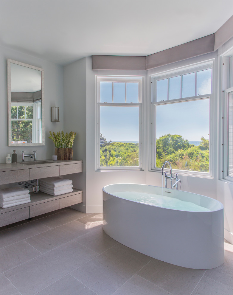 Foto di una stanza da bagno costiera con ante lisce, ante grigie, vasca freestanding, pareti bianche, lavabo integrato, pavimento grigio e top grigio