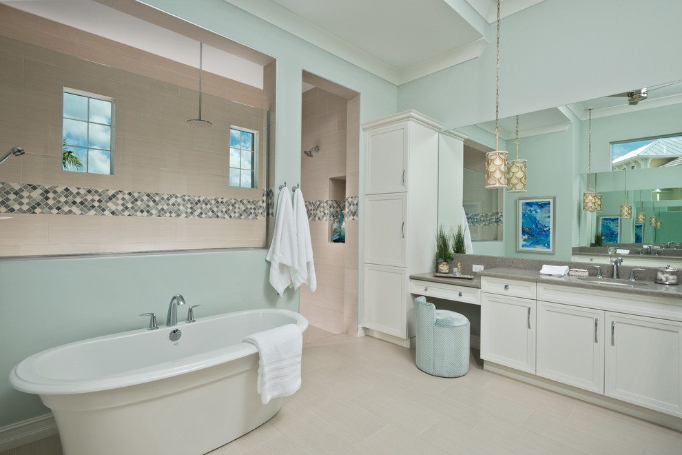 Cette photo montre une salle de bain bord de mer avec un placard avec porte à panneau encastré, des portes de placard blanches, une baignoire indépendante, un mur bleu, un lavabo encastré, un sol gris et un plan de toilette gris.