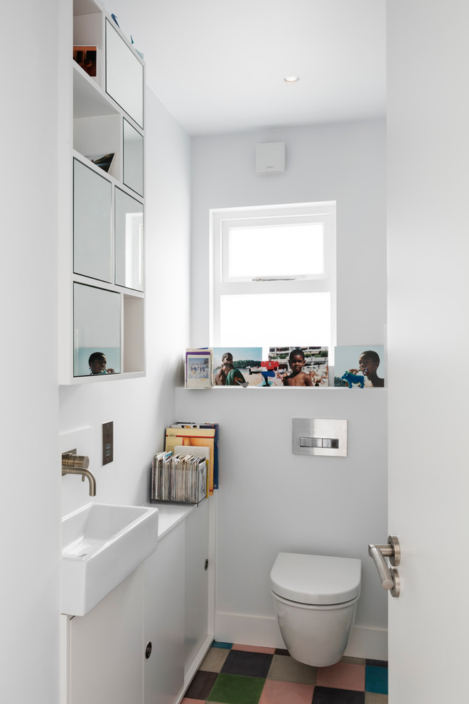 Small contemporary family bathroom in London with flat-panel cabinets, white cabinets, a wall mounted toilet, white tiles, cement tiles, white walls, ceramic flooring, a built-in sink and wooden worktops.