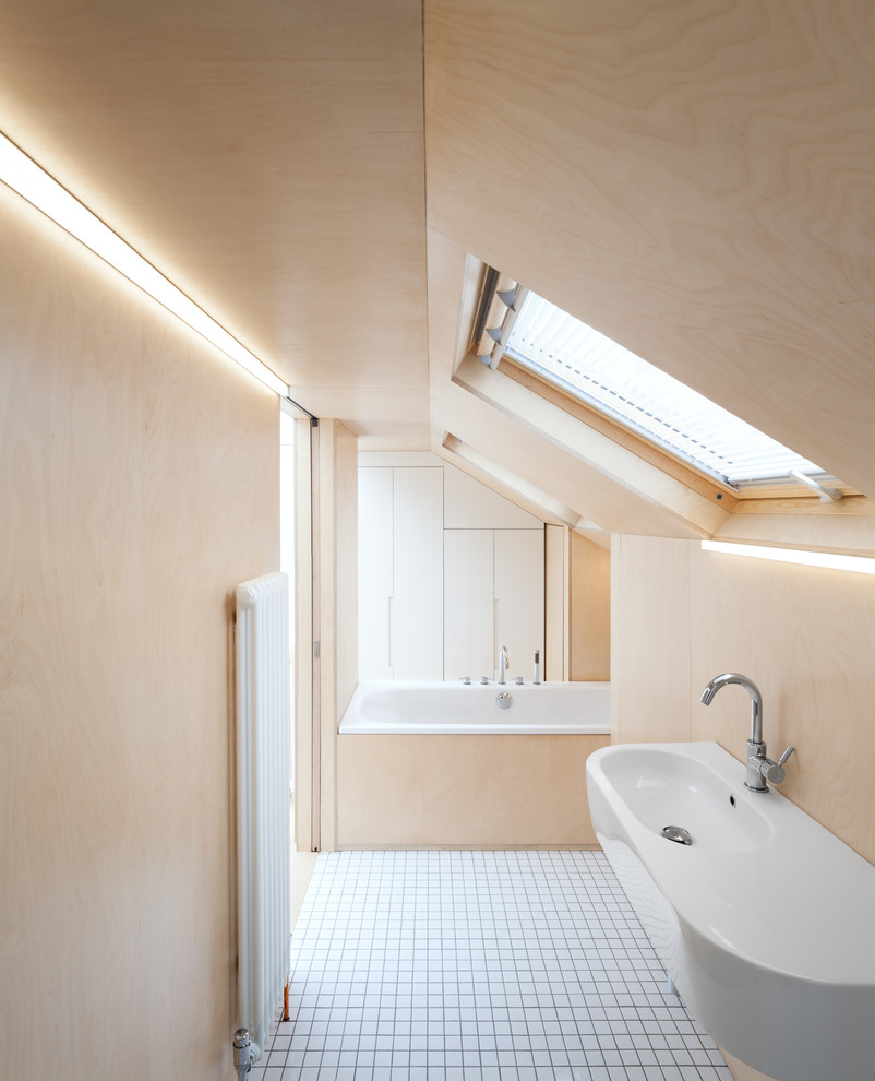 This is an example of a contemporary bathroom in London with a wall-mounted sink, a built-in bath, beige walls and ceramic flooring.