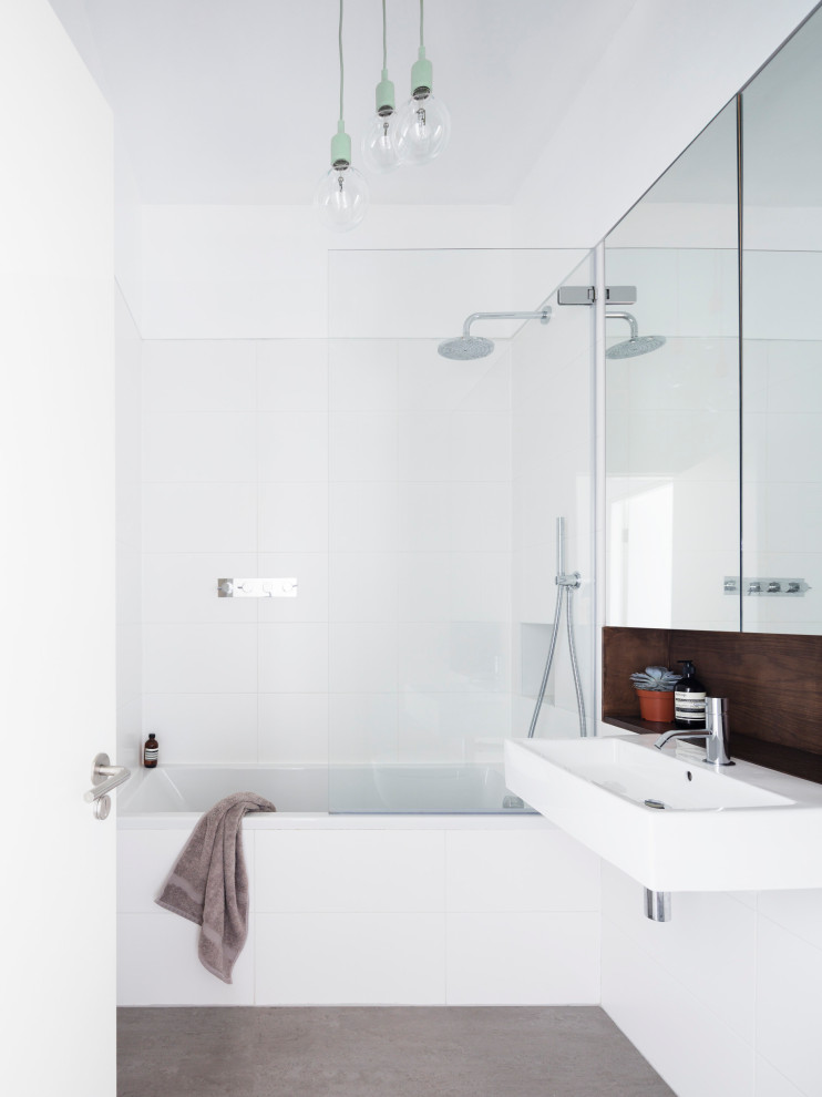 Cette image montre une salle de bain minimaliste avec une baignoire en alcôve, un combiné douche/baignoire, un carrelage blanc, un mur blanc, un lavabo suspendu, un sol gris, aucune cabine et meuble simple vasque.