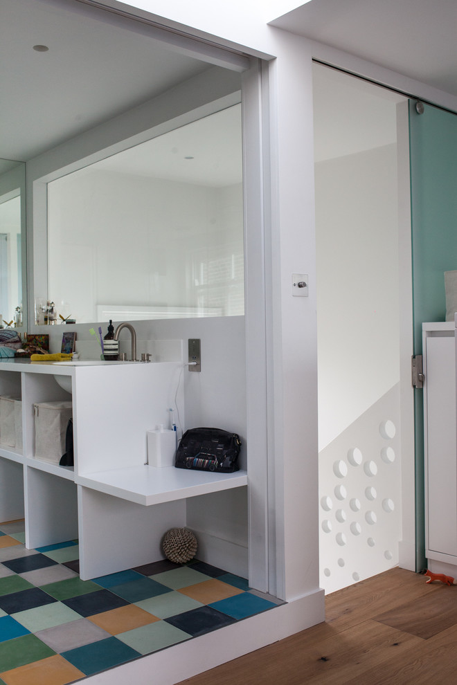 Foto på ett mellanstort funkis en-suite badrum, med ett nedsänkt handfat, öppna hyllor, vita skåp, bänkskiva i akrylsten, en kantlös dusch, flerfärgad kakel, vita väggar och ljust trägolv