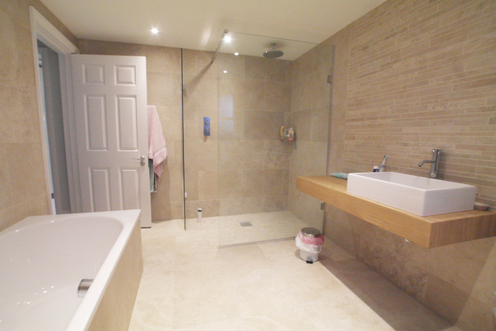 Cette image montre une salle de bain principale design de taille moyenne avec un placard à porte plane, des portes de placard grises, une baignoire posée, une douche ouverte, un carrelage beige, des carreaux de porcelaine, un lavabo suspendu et un plan de toilette en carrelage.