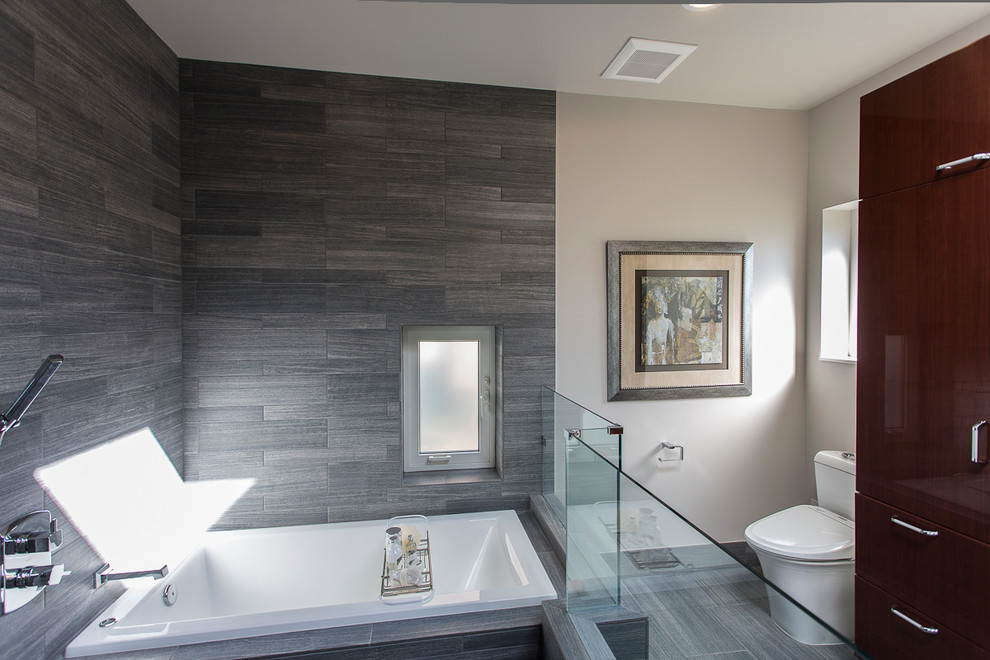 Bild på ett funkis badrum, med släta luckor, skåp i mörkt trä, ett platsbyggt badkar och grå kakel