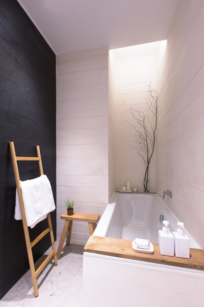 Immagine di una piccola stanza da bagno minimalista con vasca da incasso, piastrelle nere, piastrelle in pietra, pareti beige e pavimento in pietra calcarea