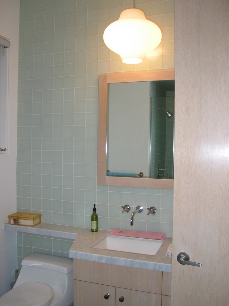 Modern inredning av ett stort en-suite badrum, med släta luckor, skåp i ljust trä, en toalettstol med hel cisternkåpa, blå kakel, glaskakel, vita väggar, ett undermonterad handfat och marmorbänkskiva