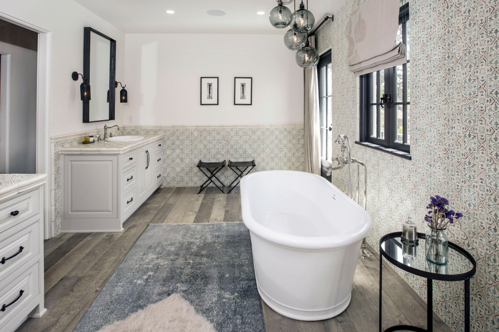 Inredning av ett medelhavsstil beige beige badrum, med luckor med upphöjd panel, vita skåp, ett fristående badkar, grå kakel, vita väggar, mellanmörkt trägolv, ett nedsänkt handfat och grått golv