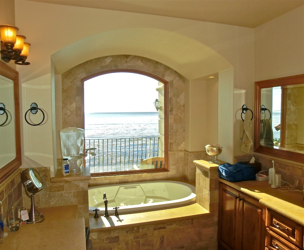 Cette image montre une grande douche en alcôve principale méditerranéenne en bois brun avec un placard avec porte à panneau surélevé, un carrelage beige, un carrelage de pierre, un mur beige, un plan de toilette en calcaire et une baignoire posée.