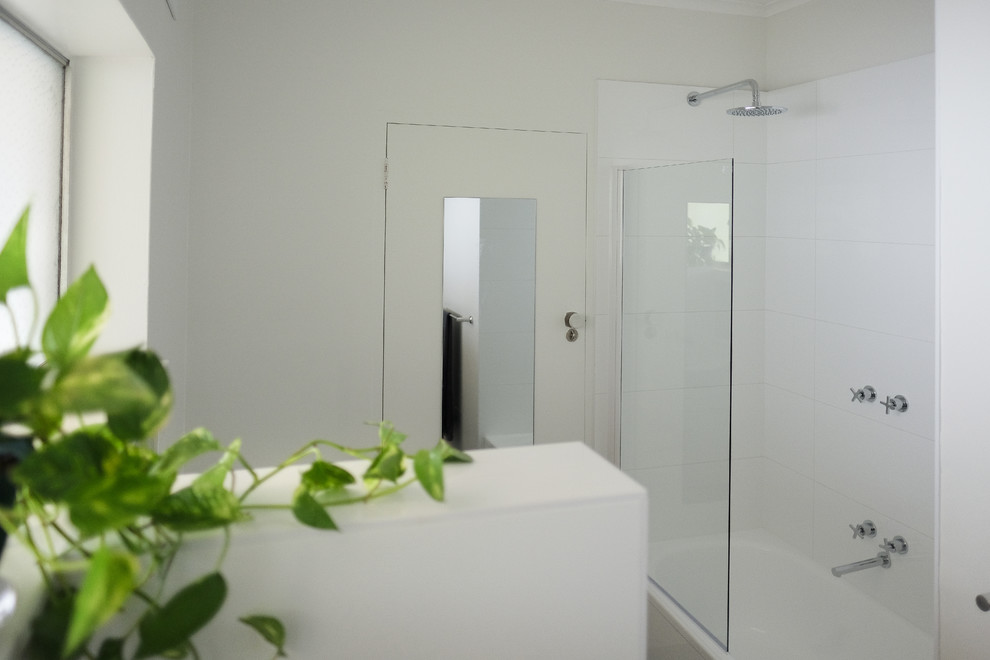 Пример оригинального дизайна: маленькая ванная комната в стиле модернизм с фасадами с утопленной филенкой, белыми фасадами, накладной ванной, душем над ванной, инсталляцией, белой плиткой, керамической плиткой, белыми стенами, полом из керамической плитки, душевой кабиной, раковиной с пьедесталом, столешницей из ламината, коричневым полом, душем с распашными дверями и белой столешницей для на участке и в саду
