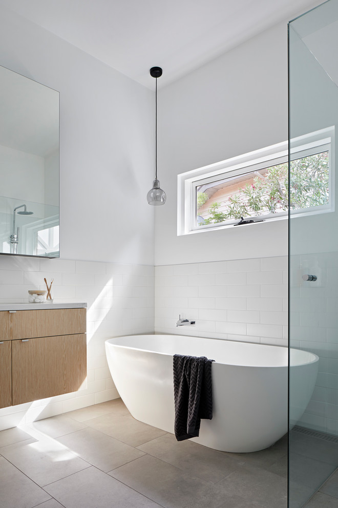 Bild på ett mellanstort funkis grå grått badrum, med ett fristående badkar, vit kakel, vita väggar, klinkergolv i porslin, bänkskiva i akrylsten och grått golv