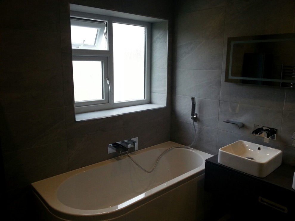 Photo of a medium sized contemporary family bathroom in Other with a wall-mounted sink, grey cabinets, laminate worktops, a walk-in shower, a wall mounted toilet, grey tiles, porcelain tiles, grey walls and porcelain flooring.