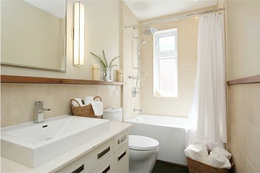 Bild på ett litet vintage en-suite badrum, med släta luckor, vita skåp, bänkskiva i kalksten, ett badkar i en alkov, en toalettstol med hel cisternkåpa, beige kakel, stenkakel, beige väggar, mörkt trägolv och ett fristående handfat