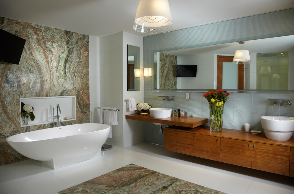 Großes Modernes Badezimmer En Suite mit verzierten Schränken, hellbraunen Holzschränken, freistehender Badewanne, Eckdusche, Toilette mit Aufsatzspülkasten, grünen Fliesen, Glasfliesen, weißer Wandfarbe, Marmorboden, Aufsatzwaschbecken, Waschtisch aus Holz, buntem Boden und Falttür-Duschabtrennung in Miami