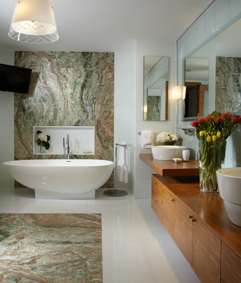 На фото: главная ванная комната в современном стиле с настольной раковиной, плоскими фасадами, фасадами цвета дерева среднего тона, отдельно стоящей ванной, разноцветной плиткой и коричневой столешницей