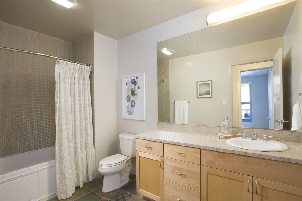 Imagen de cuarto de baño bohemio pequeño con armarios estilo shaker, puertas de armario de madera clara, bañera encastrada, combinación de ducha y bañera, sanitario de dos piezas, baldosas y/o azulejos beige, paredes grises, suelo de pizarra, lavabo encastrado y encimera de azulejos