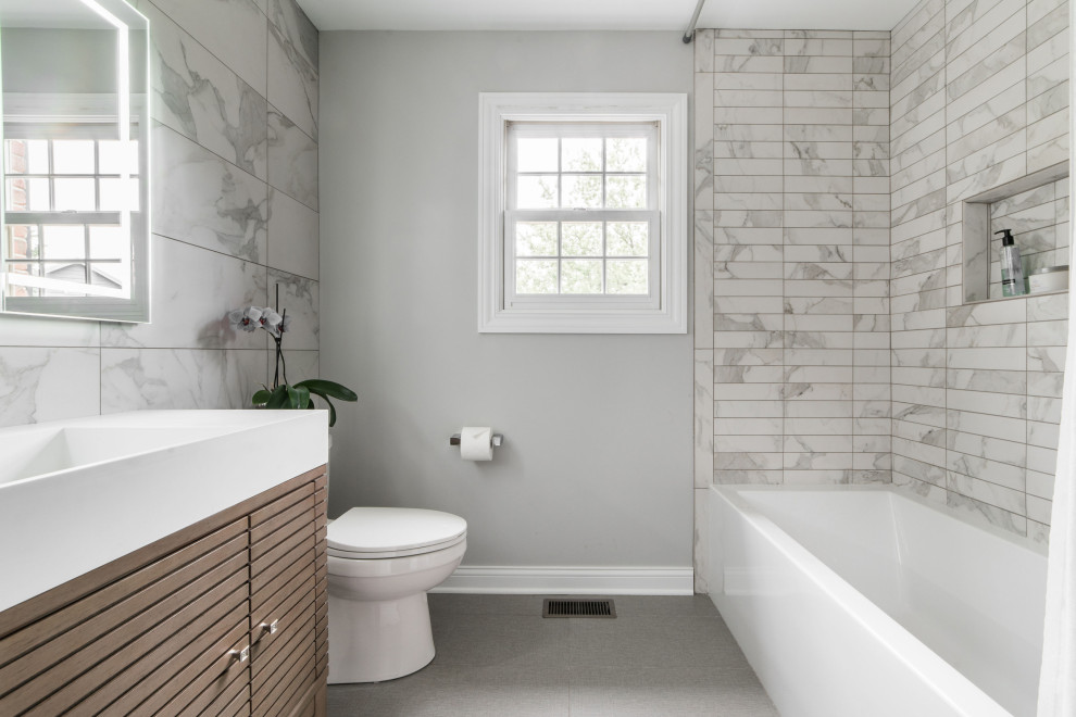 Пример оригинального дизайна: ванная комната в стиле неоклассика (современная классика) с фасадами цвета дерева среднего тона, ванной в нише, душем над ванной, раздельным унитазом, серой плиткой, белой плиткой, мраморной плиткой, серыми стенами, душевой кабиной, монолитной раковиной, шторкой для ванной, белой столешницей, тумбой под одну раковину, встроенной тумбой и плоскими фасадами