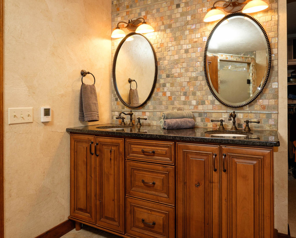 This is an example of a medium sized rustic ensuite bathroom in Minneapolis with a submerged sink, raised-panel cabinets, medium wood cabinets, granite worktops, a built-in bath, a corner shower, a one-piece toilet, multi-coloured tiles, stone tiles, beige walls and porcelain flooring.
