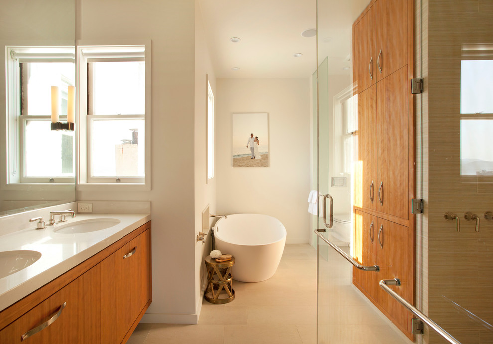 Aménagement d'une grande salle de bain principale contemporaine en bois clair avec une baignoire indépendante, un placard à porte plane, un lavabo encastré et un plan de toilette blanc.