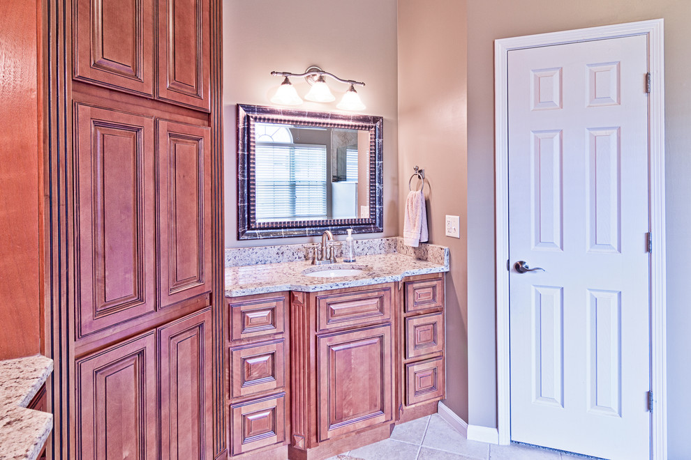 Aménagement d'une grande salle de bain principale classique en bois brun avec un lavabo encastré, un placard avec porte à panneau surélevé, un plan de toilette en granite, WC séparés, un carrelage beige, des carreaux de porcelaine, un mur beige et un sol en carrelage de porcelaine.