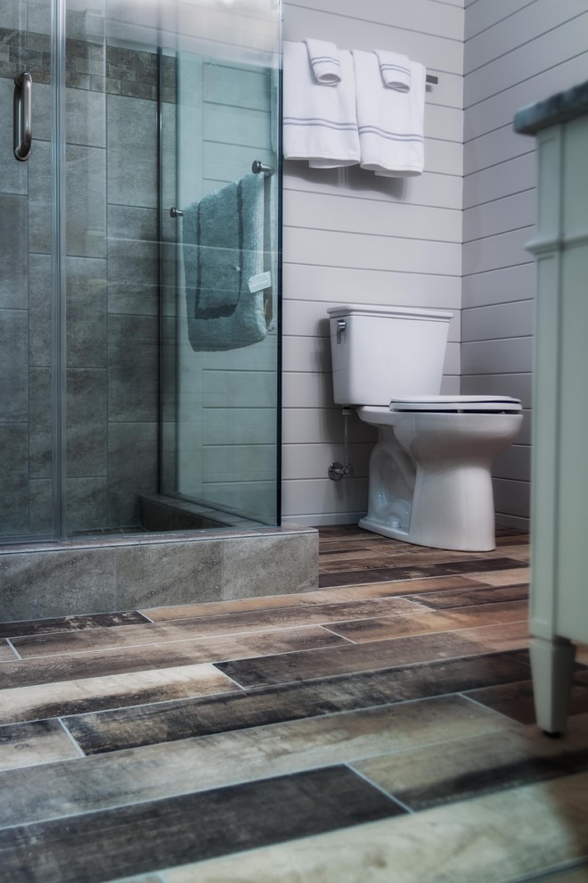 Cette photo montre une salle d'eau bord de mer de taille moyenne avec un placard avec porte à panneau encastré, des portes de placard blanches, une douche d'angle, WC séparés, un carrelage beige, des carreaux de céramique, un mur blanc, un sol en carrelage de porcelaine, un lavabo encastré, un plan de toilette en marbre, un sol marron, une cabine de douche à porte battante et un plan de toilette gris.
