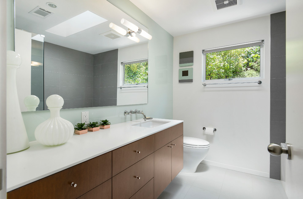 Example of a 1960s gray floor bathroom design in Los Angeles with flat-panel cabinets, dark wood cabinets, white walls, an undermount sink and white countertops