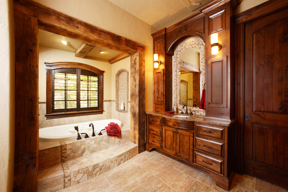 Inspiration för stora rustika en-suite badrum, med luckor med upphöjd panel, skåp i mörkt trä, ett platsbyggt badkar, kalkstensgolv, ett undermonterad handfat och granitbänkskiva