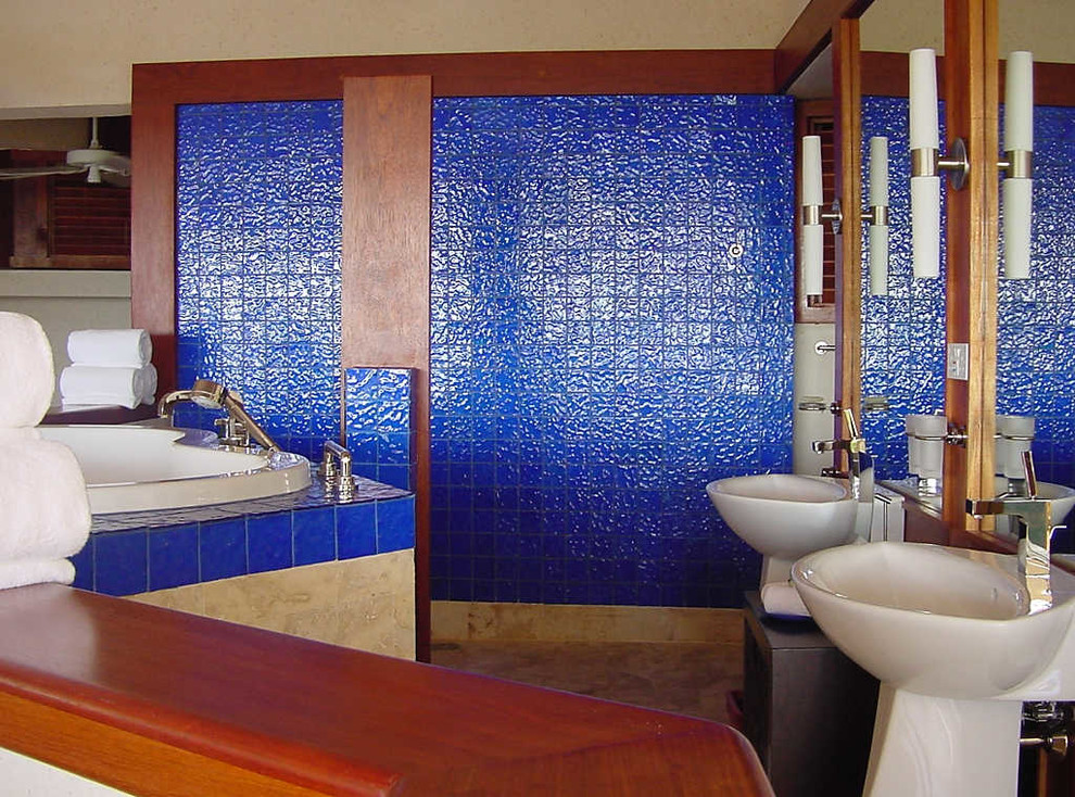 Immagine di un'ampia stanza da bagno padronale tropicale con piastrelle di vetro, lavabo a colonna, ante in legno scuro, top in legno, vasca idromassaggio, piastrelle blu, pareti blu e pavimento in travertino