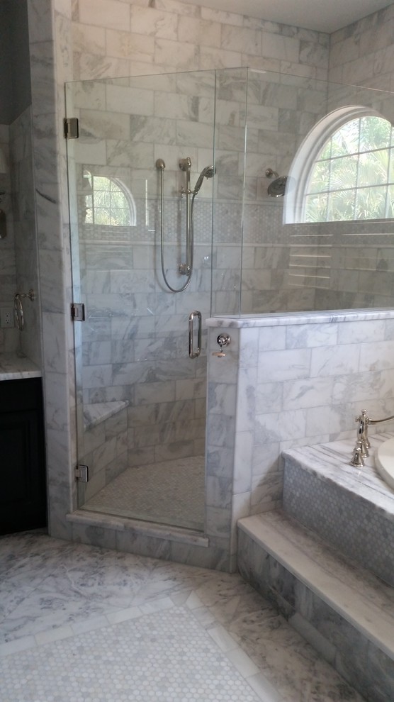 Cette image montre une salle de bain principale traditionnelle de taille moyenne avec un placard avec porte à panneau encastré, des portes de placard noires, une baignoire posée, une douche d'angle, un carrelage gris, du carrelage en marbre, un mur gris, un sol en marbre, un lavabo encastré, un plan de toilette en marbre, un sol gris et une cabine de douche à porte battante.