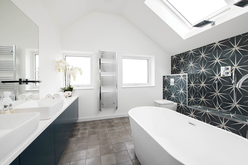 Photo of a contemporary ensuite bathroom in London with flat-panel cabinets, a freestanding bath, multi-coloured tiles, white walls, a vessel sink, grey floors, white worktops, double sinks, a floating vanity unit and a vaulted ceiling.