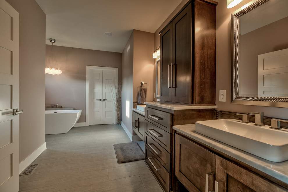 Inspiration for a large contemporary master beige tile and porcelain tile porcelain tile and gray floor bathroom remodel in Omaha with recessed-panel cabinets, dark wood cabinets, beige walls, a trough sink, solid surface countertops and a hinged shower door