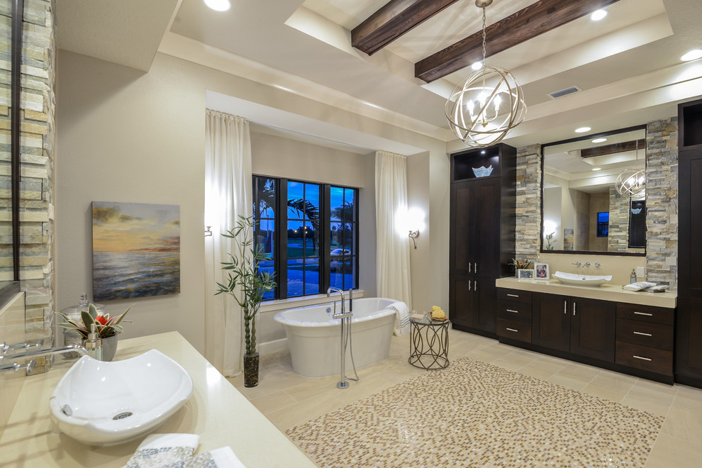 This is an example of a large mediterranean ensuite bathroom in Miami with shaker cabinets, dark wood cabinets, a freestanding bath, stone slabs, beige walls, mosaic tile flooring and a vessel sink.