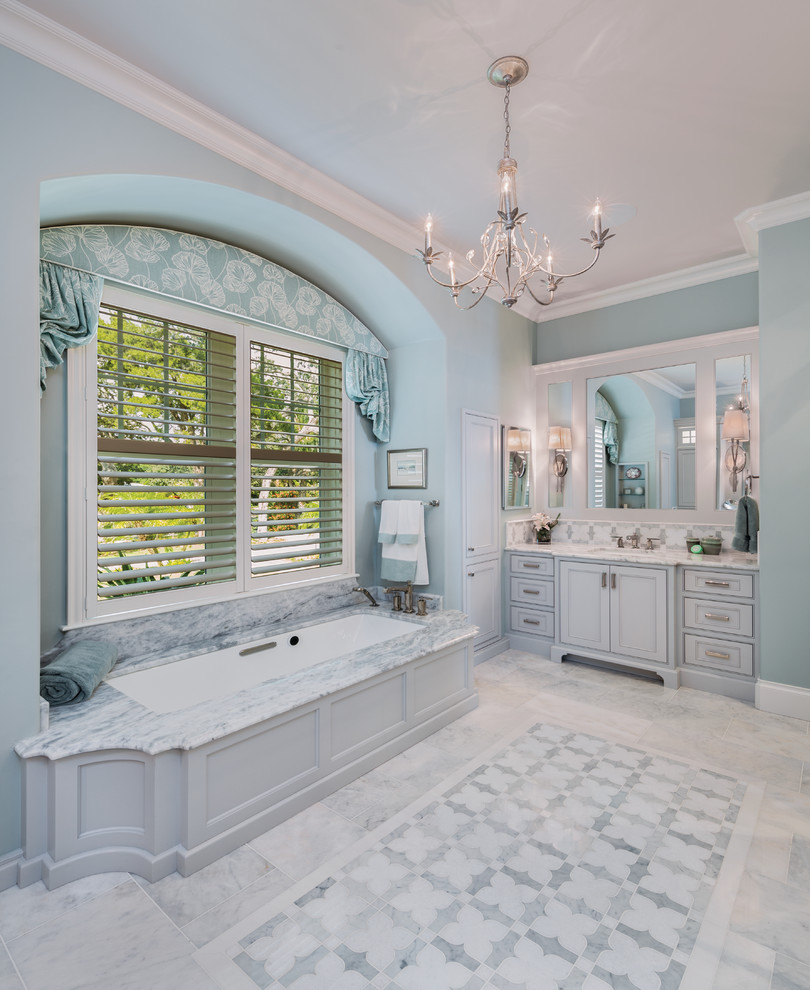 Design ideas for an ensuite bathroom in Miami with beaded cabinets, grey cabinets, an alcove bath, stone tiles, blue walls, marble flooring, a submerged sink and marble worktops.