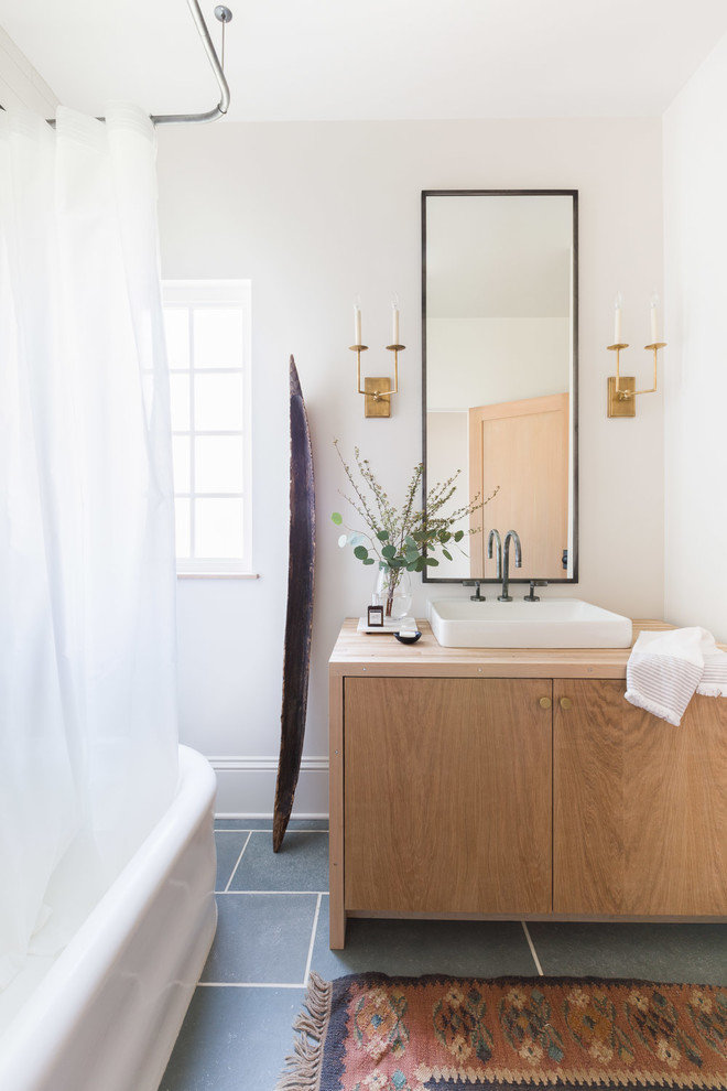 Idéer för att renovera ett lantligt brun brunt badrum med dusch, med släta luckor, skåp i ljust trä, ett fristående badkar, en dusch/badkar-kombination, vita väggar, ett fristående handfat, träbänkskiva, grått golv och dusch med duschdraperi