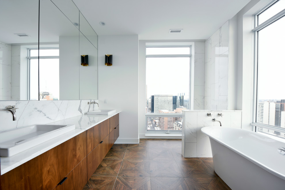 Exemple d'une salle de bain principale tendance en bois brun avec un placard à porte plane, une baignoire indépendante, un carrelage blanc, un mur blanc et un sol en bois brun.