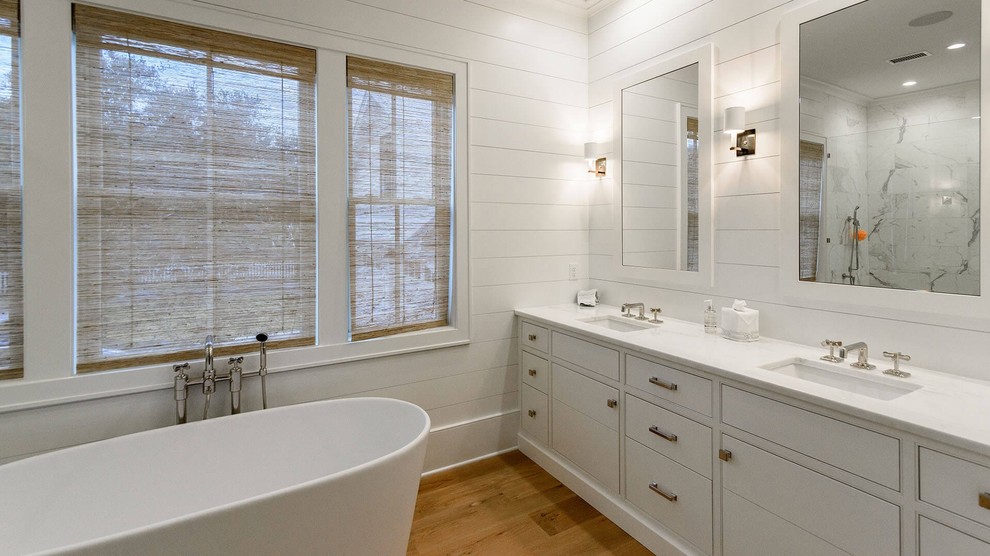 Exempel på ett stort maritimt vit vitt en-suite badrum, med släta luckor, vita skåp, ett fristående badkar, en dusch i en alkov, vit kakel, marmorkakel, vita väggar, mellanmörkt trägolv, ett undermonterad handfat, bänkskiva i kvartsit, brunt golv och dusch med gångjärnsdörr