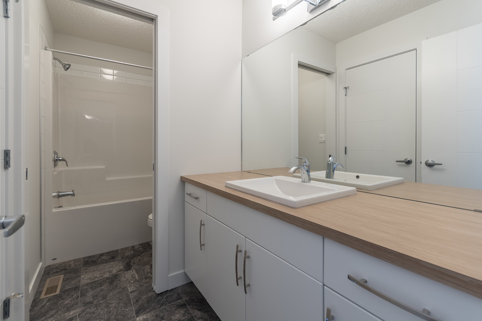 This is an example of a medium sized contemporary family bathroom in Edmonton with flat-panel cabinets, white cabinets, an alcove bath, a one-piece toilet, white tiles, metro tiles, white walls, ceramic flooring, a built-in sink, laminate worktops and grey floors.