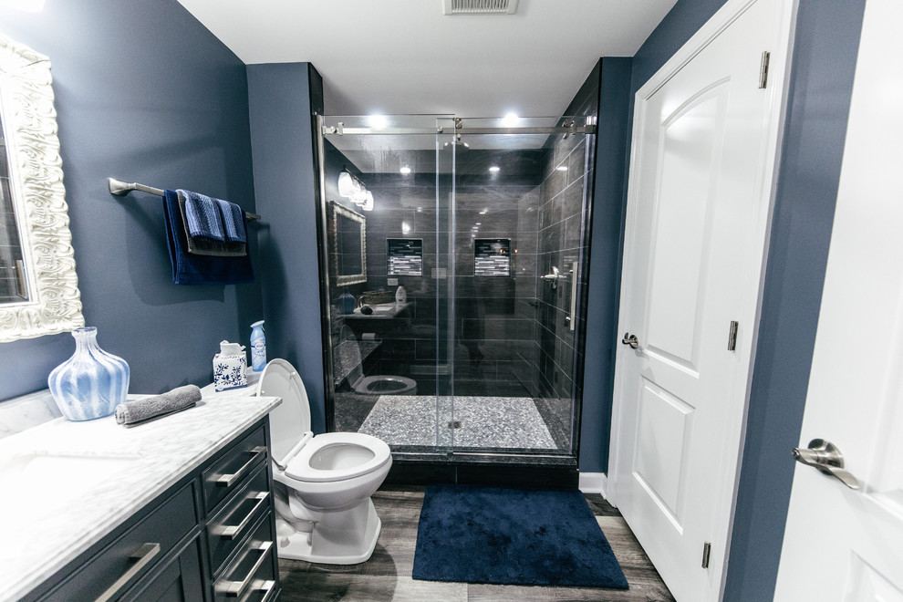 Пример оригинального дизайна: ванная комната среднего размера в стиле модернизм с фасадами в стиле шейкер, серыми фасадами, душем в нише, унитазом-моноблоком, серой плиткой, керамогранитной плиткой, синими стенами, полом из ламината, душевой кабиной, врезной раковиной, столешницей из искусственного кварца, серым полом, душем с раздвижными дверями и белой столешницей