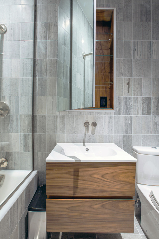 Idéer för mellanstora funkis beige en-suite badrum, med släta luckor, skåp i mellenmörkt trä, ett platsbyggt badkar, en dusch/badkar-kombination, en toalettstol med hel cisternkåpa, grå kakel, porslinskakel, grå väggar, klinkergolv i porslin, ett integrerad handfat, grått golv, med dusch som är öppen och marmorbänkskiva