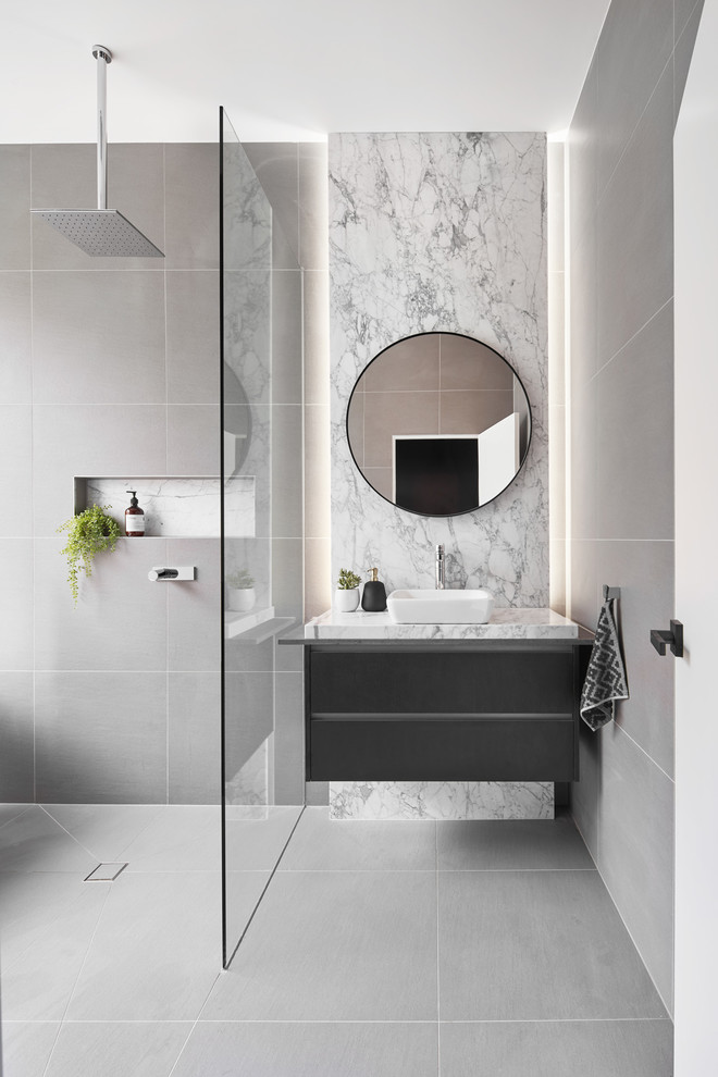 Exempel på ett mellanstort modernt vit vitt en-suite badrum, med möbel-liknande, svarta skåp, ett fristående badkar, en öppen dusch, en vägghängd toalettstol, grå kakel, stenhäll, vita väggar, klinkergolv i porslin, ett konsol handfat, marmorbänkskiva, grått golv och med dusch som är öppen