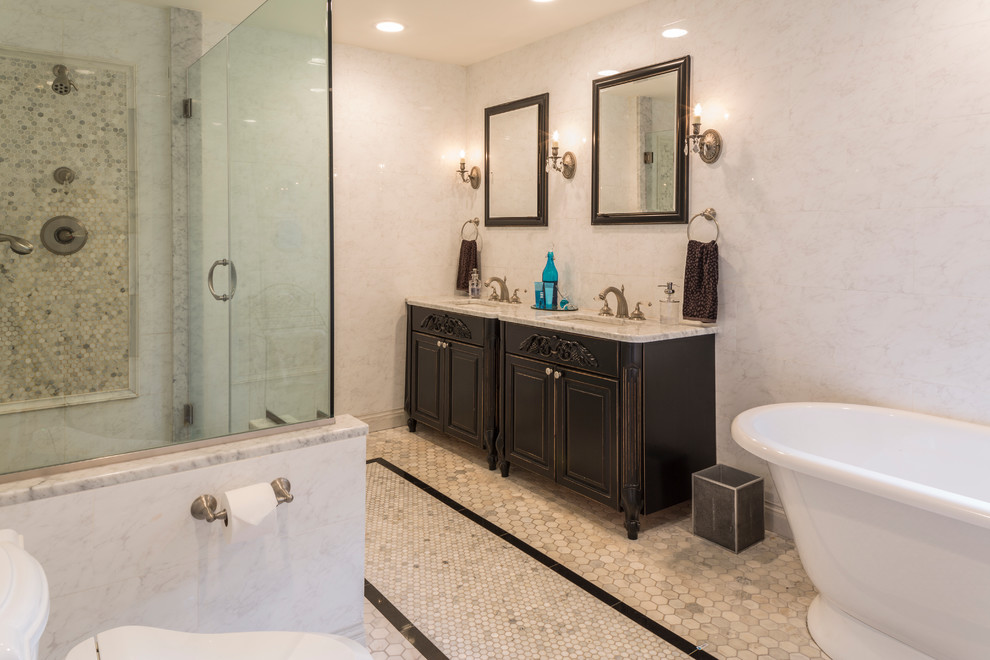 Medium sized traditional ensuite bathroom in New York with freestanding cabinets, dark wood cabinets, a freestanding bath, a corner shower, a two-piece toilet, beige walls, marble flooring, a submerged sink, beige floors and a hinged door.