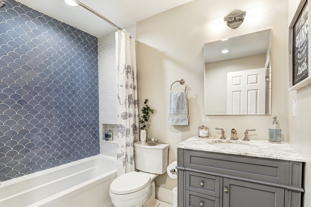 На фото: детская ванная комната среднего размера в стиле неоклассика (современная классика) с фасадами в стиле шейкер, серыми фасадами, ванной в нише, душем над ванной, раздельным унитазом, синей плиткой, керамической плиткой, серыми стенами, полом из керамической плитки, врезной раковиной, мраморной столешницей, шторкой для ванной и белой столешницей с