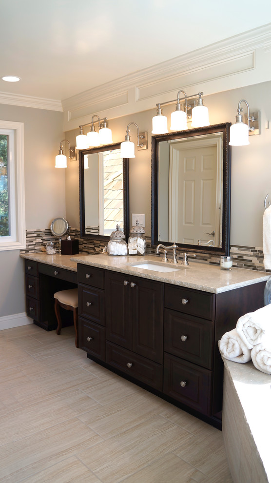 This is an example of a large traditional ensuite bathroom in Seattle with a submerged sink, raised-panel cabinets, dark wood cabinets, limestone worktops, a corner bath, a double shower, a one-piece toilet, beige tiles, porcelain tiles, beige walls and porcelain flooring.