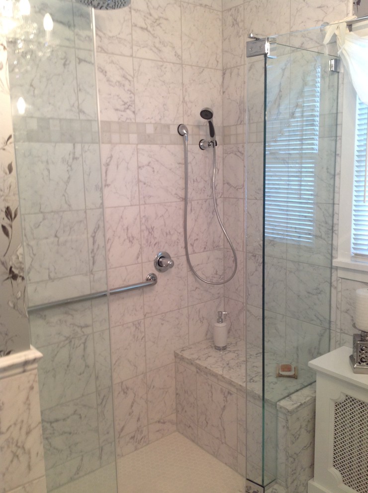 Klassisk inredning av ett badrum, med ett undermonterad handfat, luckor med infälld panel, vita skåp, marmorbänkskiva, en dusch i en alkov, en toalettstol med hel cisternkåpa, vit kakel, stenkakel och marmorgolv