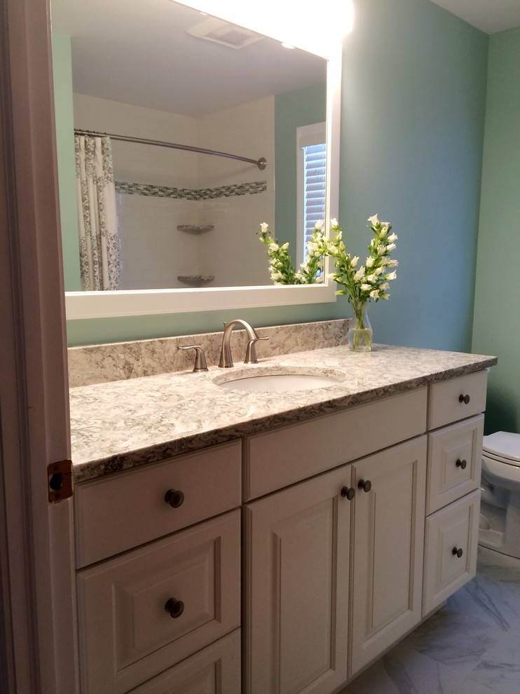 Photo of a medium sized classic family bathroom in New York with raised-panel cabinets, white cabinets, an alcove bath, a two-piece toilet, white tiles, glass tiles, green walls, porcelain flooring, a submerged sink and quartz worktops.