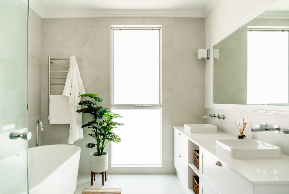 Cette photo montre une salle de bain tendance avec un placard à porte shaker, des portes de placard blanches, une baignoire indépendante, un lavabo posé, un sol blanc, un plan de toilette blanc, meuble double vasque et meuble-lavabo encastré.