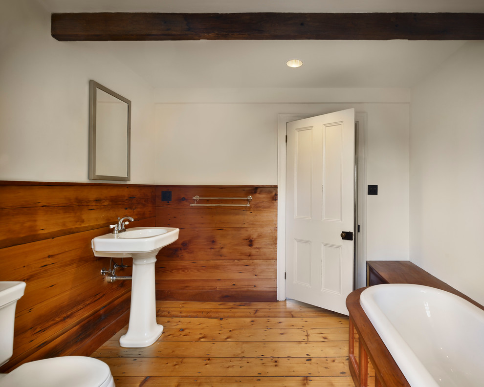 This is an example of a medium sized traditional ensuite bathroom in New York with a freestanding bath, a two-piece toilet, white walls, dark hardwood flooring, a pedestal sink and brown floors.