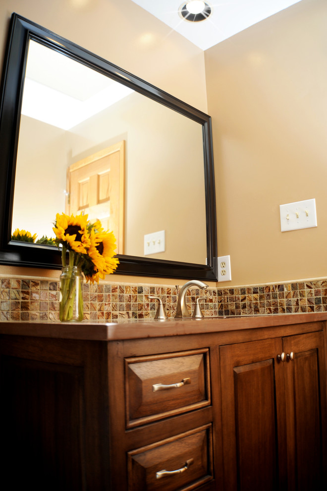 Bild på ett amerikanskt badrum, med ett undermonterad handfat, luckor med upphöjd panel, skåp i mellenmörkt trä, beige kakel, mosaik och beige väggar