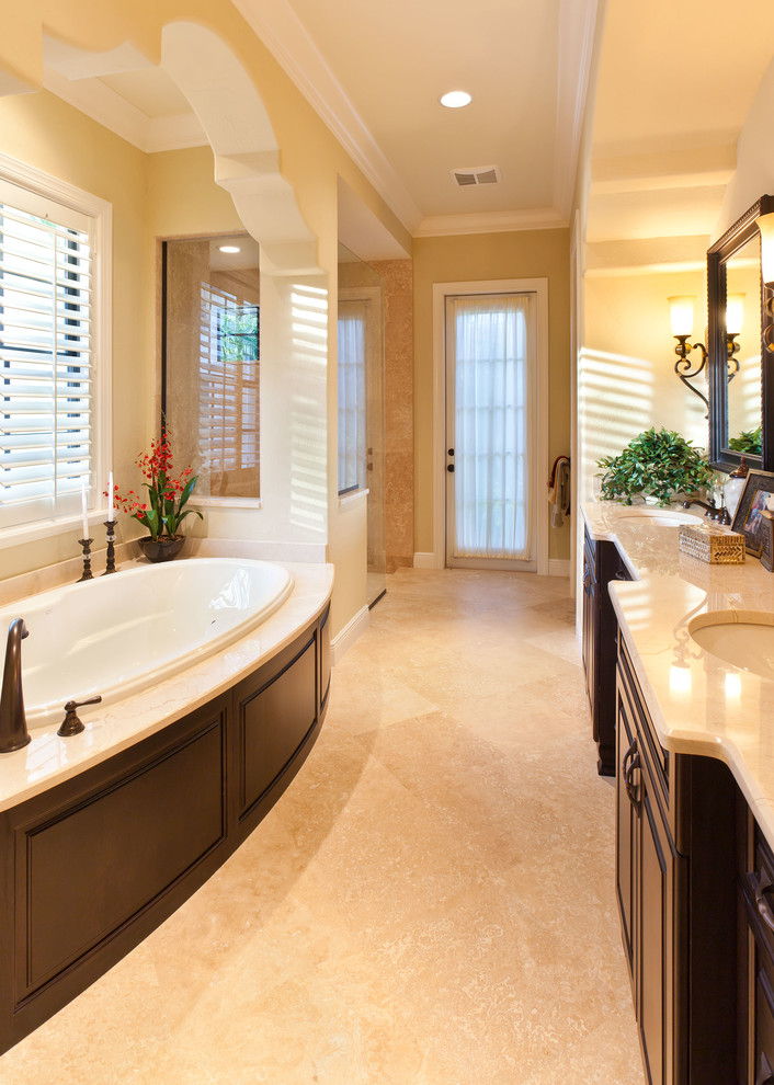 Example of a huge tuscan master beige tile and stone tile limestone floor bathroom design in Tampa with an undermount sink, raised-panel cabinets, dark wood cabinets, marble countertops, a two-piece toilet and yellow walls